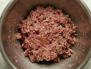 Fully mixed Biff à la Lindström meat mixture in a metal bowl with visible beetroot and capers