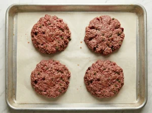 Four raw Biff à la Lindström patties shaped on a parchment-lined sheet pan