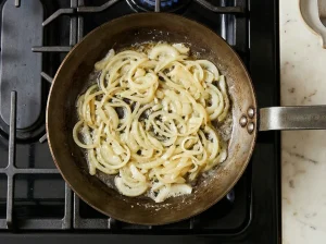 Thinly sliced yellow onions cooking in a skillet on a stovetop until soft and translucent.