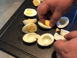 A person’s hands separating cooked yellow yolks from hard-boiled egg whites on a black cutting board while preparing Finnish Munavoi.