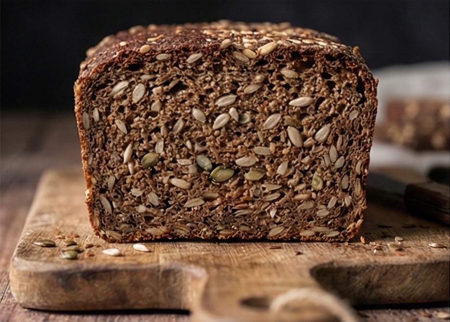 Close-up of a Danish rugbrød slice showing a dense crumb packed with sunflower and pumpkin seeds.