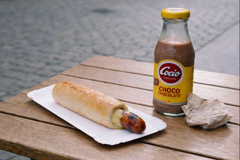 Fransk hot dog (Danish sausage in a baguette) on a paper tray with a bottle of Cocio chocolate milk on a wooden table in Copenhagen, Denmark.