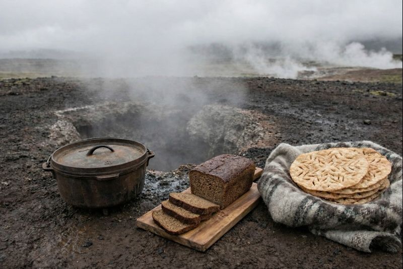 A cast-iron pot sitting on steaming volcanic ground, next to a freshly unburied, dark, crustless loaf of Icelandic rye bread.
