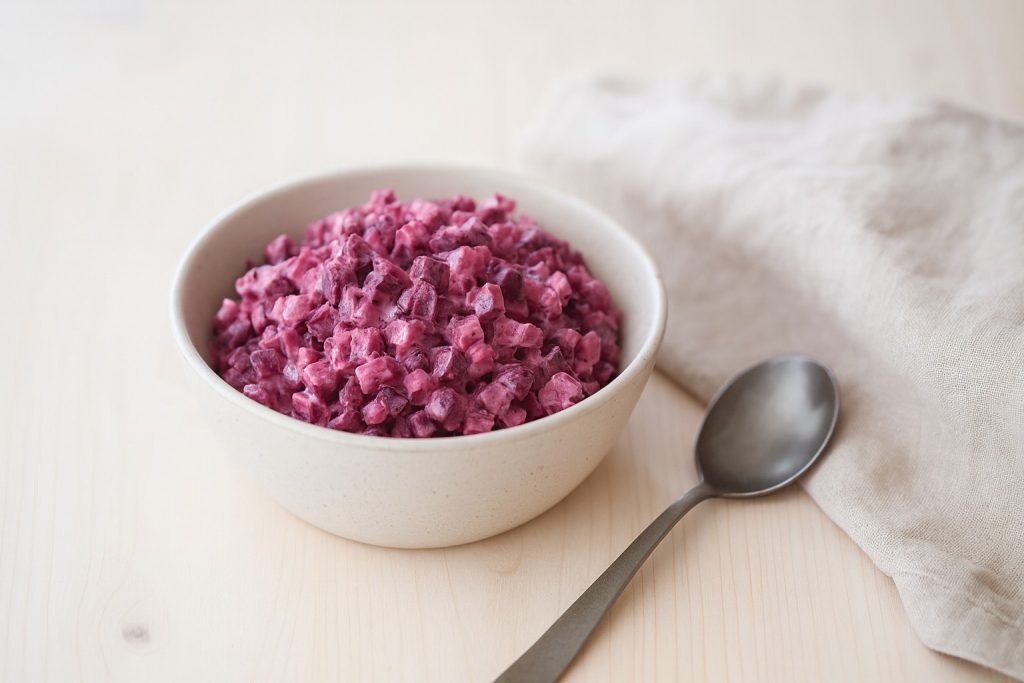 Nordic beetroot salad in a modern ceramic bowl on a light wooden table with a beige linen napkin and spoon, photographed in soft Scandinavian daylight.