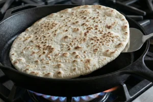 Flipped flatbread showing characteristic brown toasted spots on the surface.