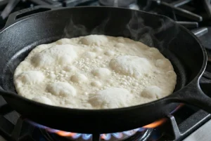 Flatbread cooking in a dry cast-iron skillet, turning opaque with small bubbles.