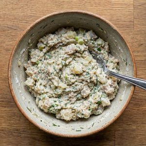 A bowl of prepared Danish fish cake mixture made with white fish, onions, herbs, and cream, showing the soft and cohesive texture before chilling.