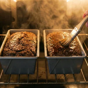 Brushing syrup glaze over saaristolaisleipä loaves while baking in the oven.