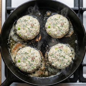 Pan-frying Danish fish cakes in a mixture of butter and oil over medium heat, leaving space between each patty.
