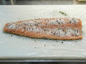 A salmon fillet covered in a coarse curing mixture of salt, sugar, and crushed spices.