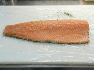 A fresh, raw salmon fillet placed skin-side down on a large sheet of plastic wrap, ready for seasoning.