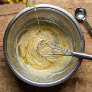 Whisking hovmästarsås while slowly drizzling in oil to form a creamy emulsion in a mixing bowl.