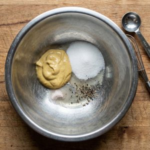Ingredients for Swedish hovmästarsås in a mixing bowl—mustard, sugar, salt, and black pepper.