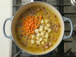 Diced carrots and potatoes added to simmering pea soup in a Dutch oven
