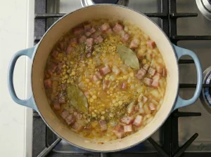 Bay leaves and herbs simmering with split peas, onions, and ham in a pot
