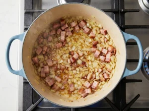 Diced onions and ham sautéing in a Dutch oven
