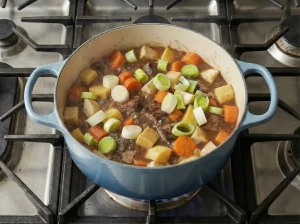 Sliced leeks and potatoes added on top of the simmering Norwegian beef stew lapskaus in a Dutch oven.