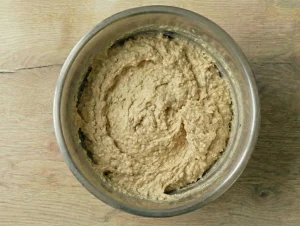 A thick, grainy cake batter in a stainless steel bowl, showing the characteristic texture of the almond meal and breadcrumbs.