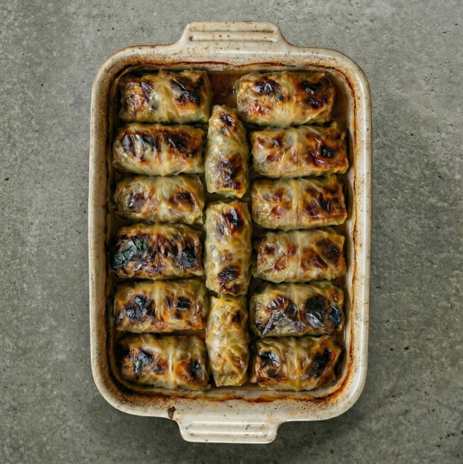 Top-down view of baked Swedish cabbage rolls (kåldomar) in a ceramic baking dish.