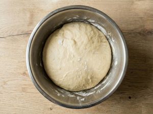 Risen semla dough expanded in a stainless-steel bowl, lightly dusted with flour.
