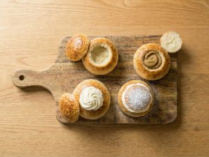 Semla buns in different assembly stages—hollowed, filled with almond paste, topped with whipped cream, and dusted with powdered sugar.