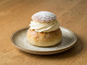 Finished Swedish semla with whipped cream and powdered sugar served on a rustic plate on a wooden table.