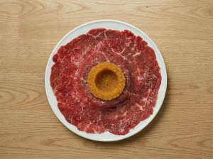 Raw egg yolk placed on top of löjrom and paper-thin beef tenderloin on toast for Toast Pelle Janzon assembly