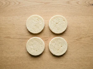 Four round white bread circles cut to 3-inch diameter for Toast Pelle Janzon, laid out on a wooden surface