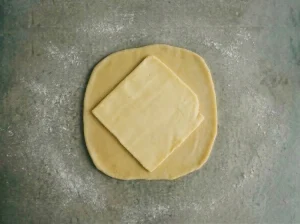 A cold butter block placed diagonally in the center of rolled-out Danish pastry dough, ready to be folded and encased