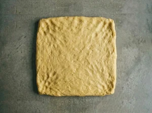 Danish pastry dough patted into a thick square before refrigerating, viewed from above on a gray kitchen counter