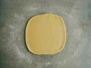 Laminated Danish pastry dough rolled into a smooth square on a lightly floured table surface, ready to encase the butter block