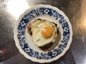 A completed Swedish Operasmörgås topped with a fried egg on a decorative blue and white plate.
