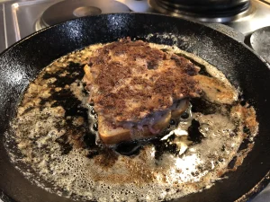 The sandwich flipped over in a skillet, showing a browned meat patty and toasting bread.