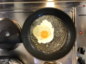 A single egg frying sunny-side up in a pan for a sandwich topping.