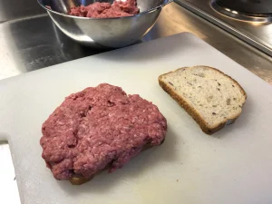 Pressing raw ground beef mixture onto a slice of white sandwich bread.